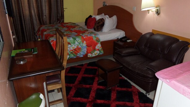 A hotel room with a bed, a desk, a chair, a couch, and a small table. - Koltol Guest House (Ibadan)