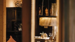 Un comedor con una mesa de madera dispuesta para dos personas, un espejo que refleja la habitación y una zona de estar acogedora con un cojín.
