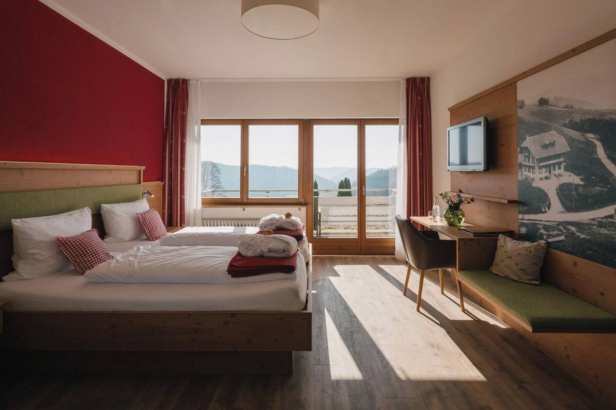 Quarto de hotel com uma cama grande, uma escrivaninha, uma televisão e vista para as montanhas.