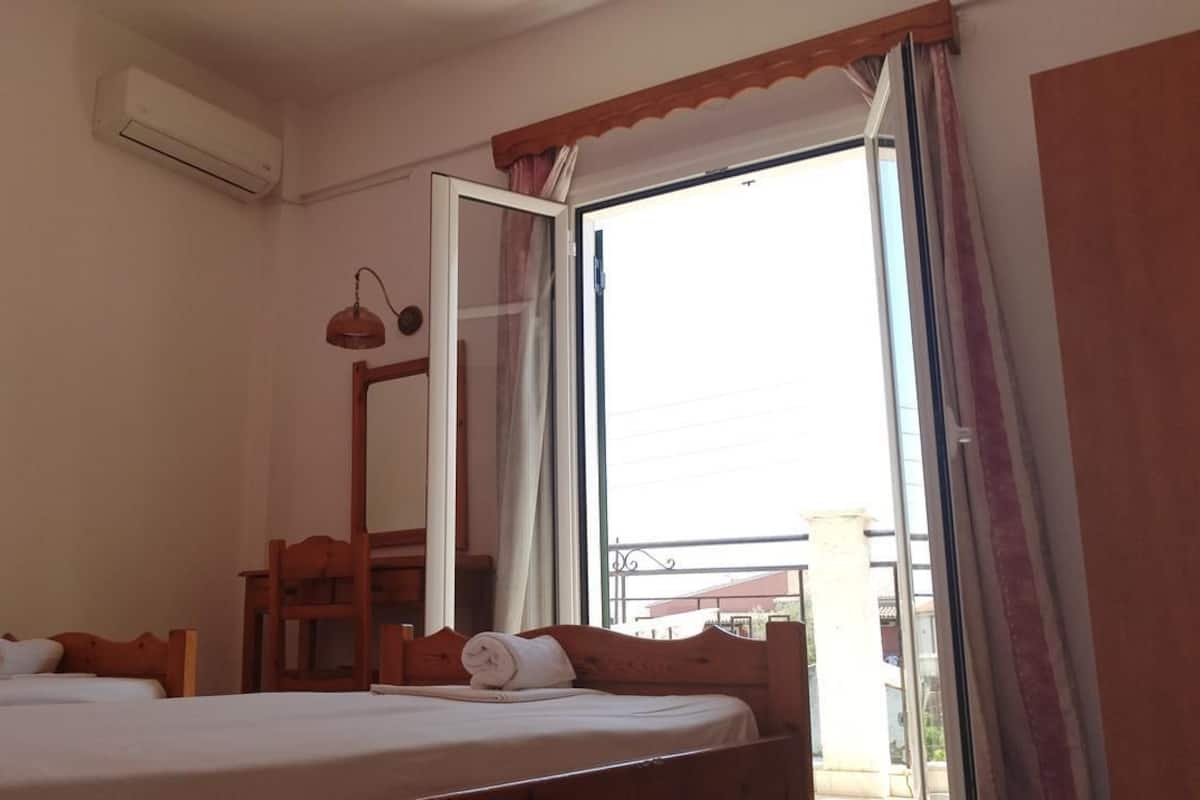 Ein Zimmer mit zwei Betten, einem Fenster mit Vorhängen, einem Spiegel und einer Klimaanlage.