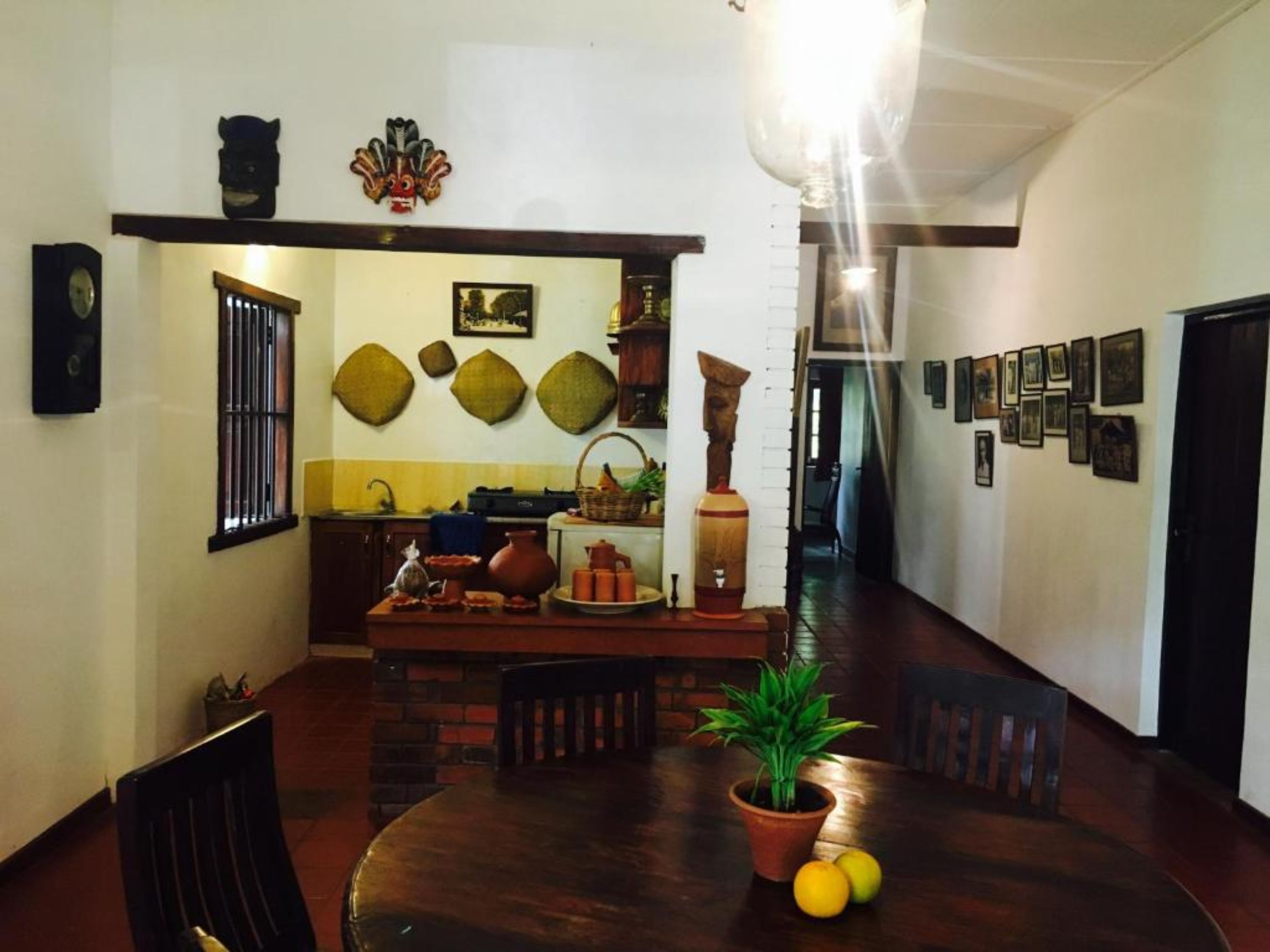 A dining area with a wooden table, chairs, a potted plant, and a kitchen in the background.