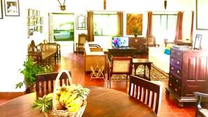 Una sala de estar bien iluminada con televisión, una mesa de comedor con una cesta de fruta y una estantería.
