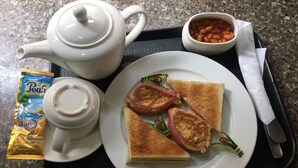 Un vassoio con teiera, tazza, piatto con pane tostato e fette di pomodoro, ciotola di fagioli e una confezione di latte.