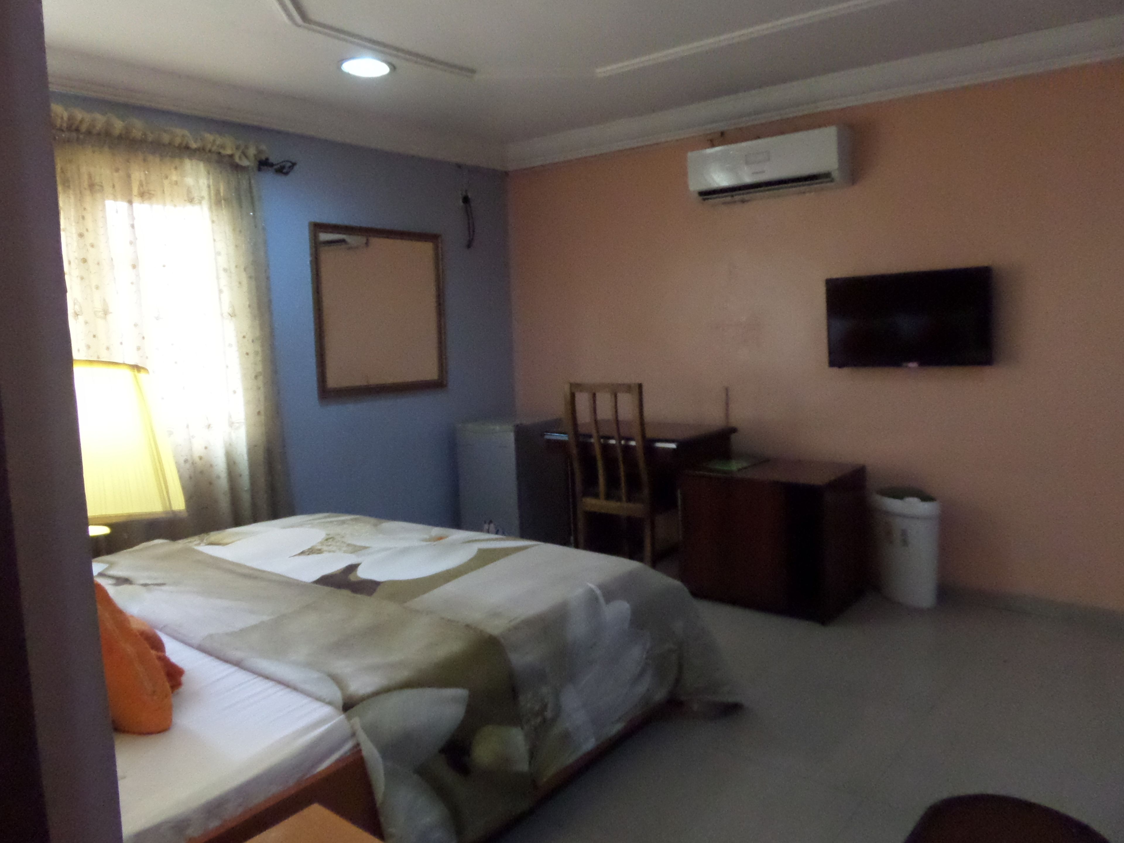 Habitación de hotel con cama, escritorio, silla, aire acondicionado y televisor en la pared.