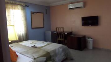 Habitación de hotel con cama, escritorio, silla, aire acondicionado y televisor en la pared.