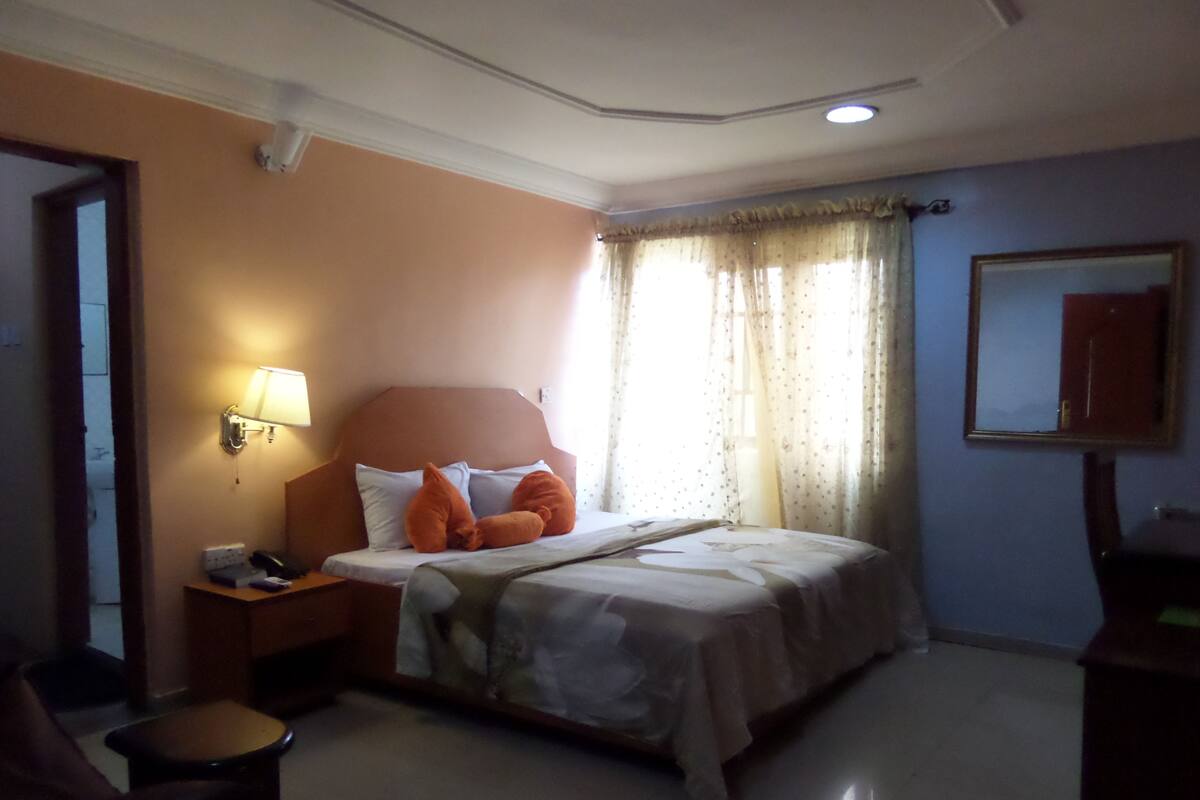 A hotel room with a bed, a nightstand, a chair, and a mirror.