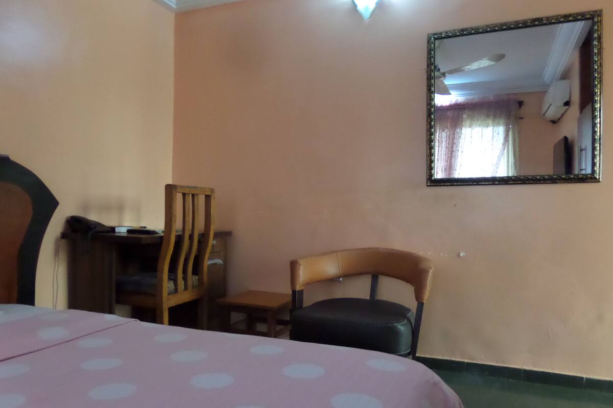 A room with a bed, a desk, a chair, and a mirror on the wall.