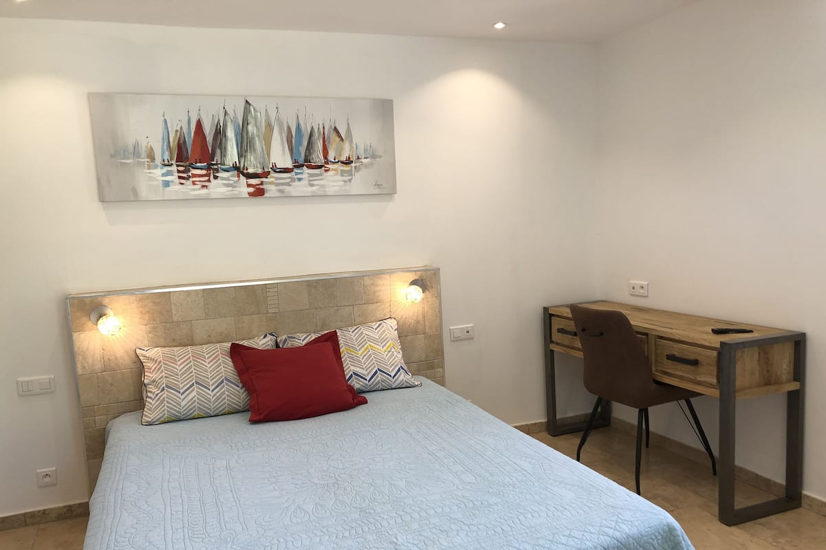 Quarto com cama, escrivaninha e pintura de veleiros.