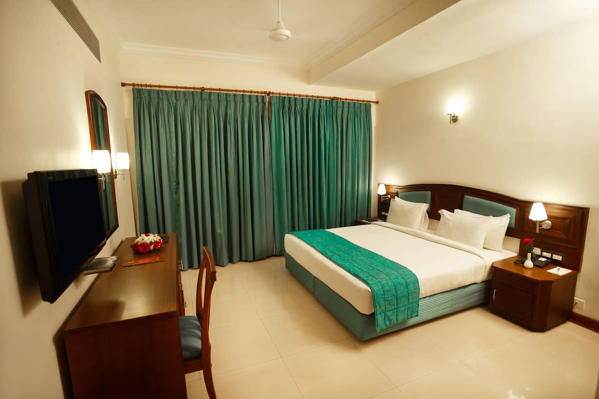 A hotel room with a bed, bedside table, lamp, TV, and a desk with a chair.