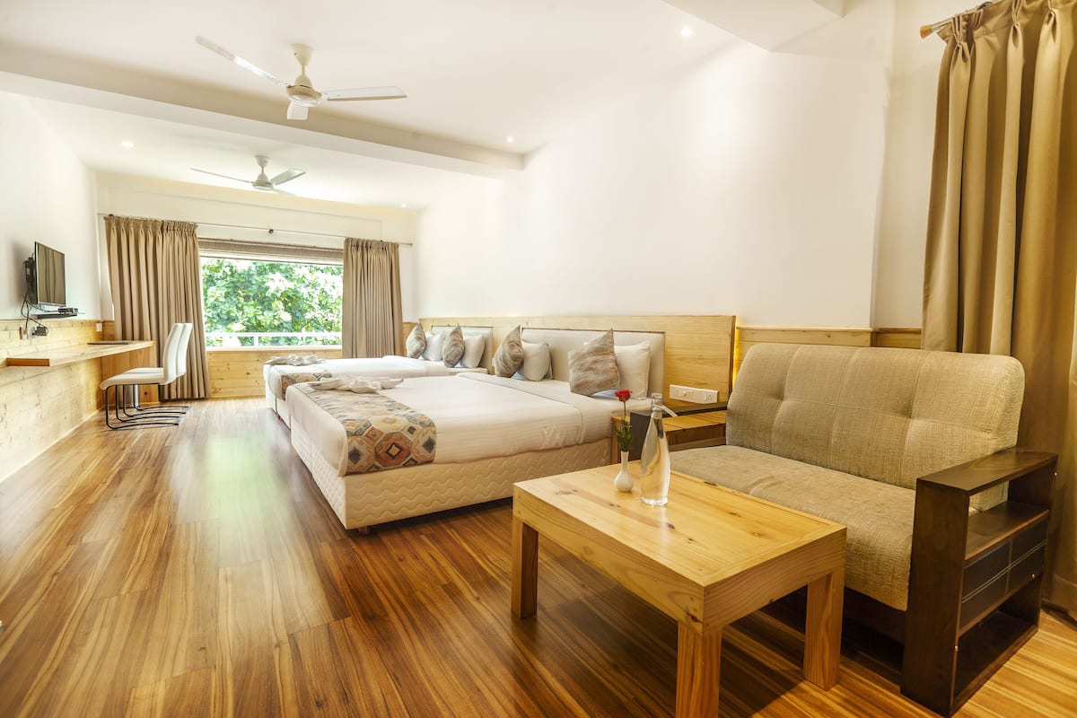 A modern hotel room with a large bed, a sofa, a wooden coffee table, a desk, and a TV.