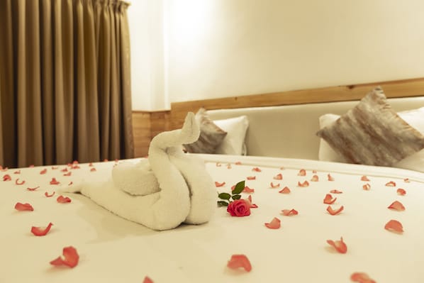 A bed with rose petals and a swan-shaped towel, a wooden headboard, and a pillow with a textured design.