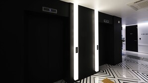 A modern hallway with black doors, illuminated by overhead lights, and a patterned floor. - Hotel yaja wirye (Seongnam)