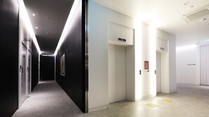A modern hotel corridor with a long hallway, doors numbered 1013 and 1014, and an elevator with a sign indicating floors 1001-1006. - Hotel yaja wirye (Seongnam)