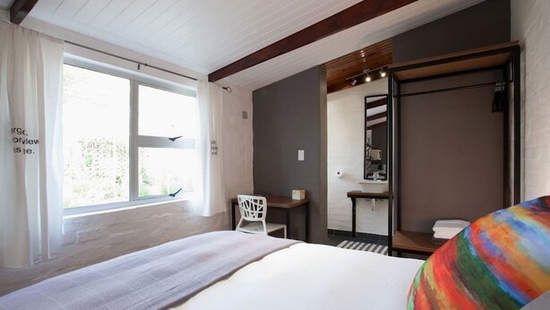 A bedroom with a bed, a desk, a chair, and a large window. - Lemon tree Studio Stellenbosch Central (Stellenbosch)