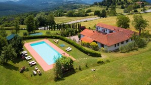 A large house with a swimming pool surrounded by lawn chairs and a tennis court.