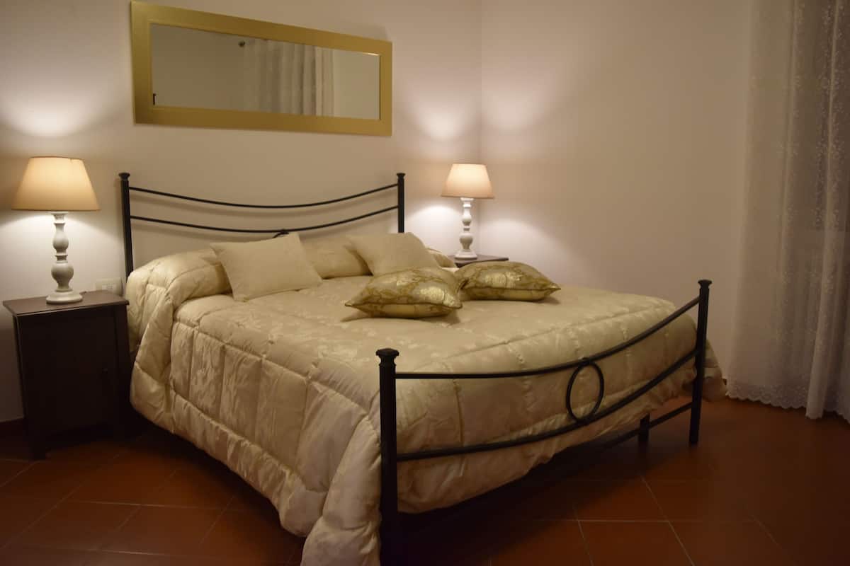 Un lit bien fait, avec une tête de lit, deux tables de chevet dotées de lampes et un miroir au-dessus du lit.