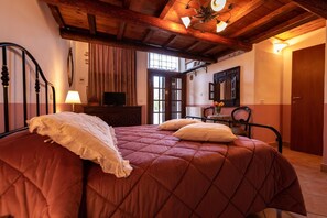 A bedroom with a large bed, wooden ceiling beams, a television, and a window.