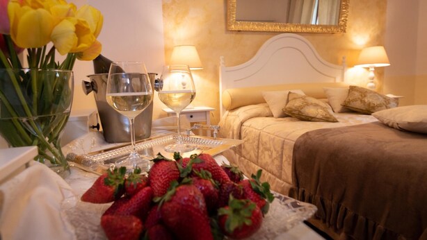 A hotel room with a bed, bedside lamps, a tray with strawberries, a wine glass, and a vase with yellow flowers.