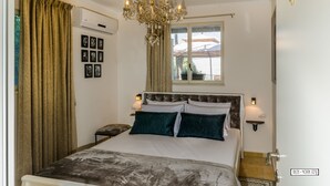 Un dormitorio con cama, candelabro, ventana con cortinas, luces empotradas en la pared y una mesita de noche pequeña.