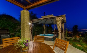 An outdoor patio with a hot tub, wooden deck, and a table with flowers. - Naomi's (Rosh Pinna)
