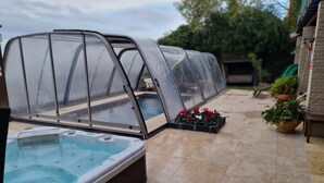 Una piscina techada con un jacuzzi, rodeada de plantas en macetas y un muro de ladrillo.