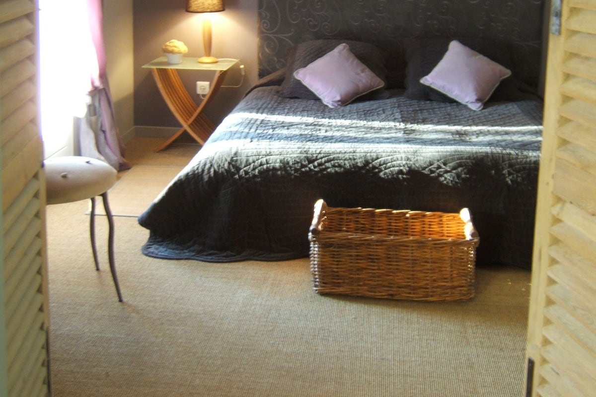A bedroom with a bed, a nightstand, a lamp, a chair, and a wicker basket.