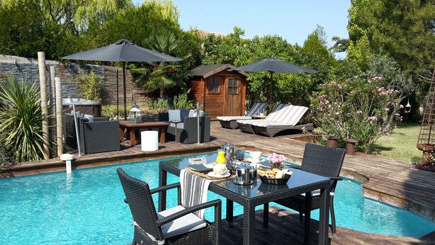 A poolside area with a dining table, chairs, lounge chairs, and umbrellas. - Chambres d'Hôtes de la Ferrage (La Tour-d'Aigues)