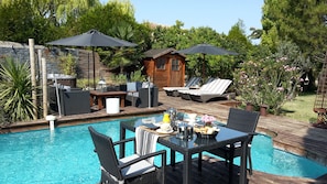 A poolside area with a dining table, chairs, lounge chairs, and umbrellas.