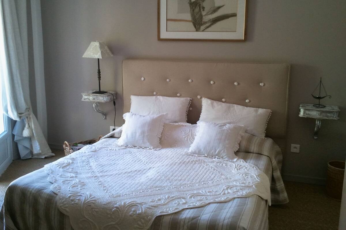 A neatly made bed with a striped bedspread and multiple pillows, a bedside table with a lamp, and a framed artwork on the wall.