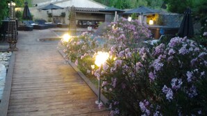 A wooden pathway leading to a building with outdoor seating and a garden with pink flowers. - Chambres d'Hôtes de la Ferrage (La Tour-d'Aigues)