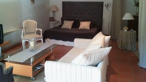 A hotel room with a bed, a sofa, a chair, a small table, and a TV. - Chambres d'Hôtes de la Ferrage (La Tour-d'Aigues)