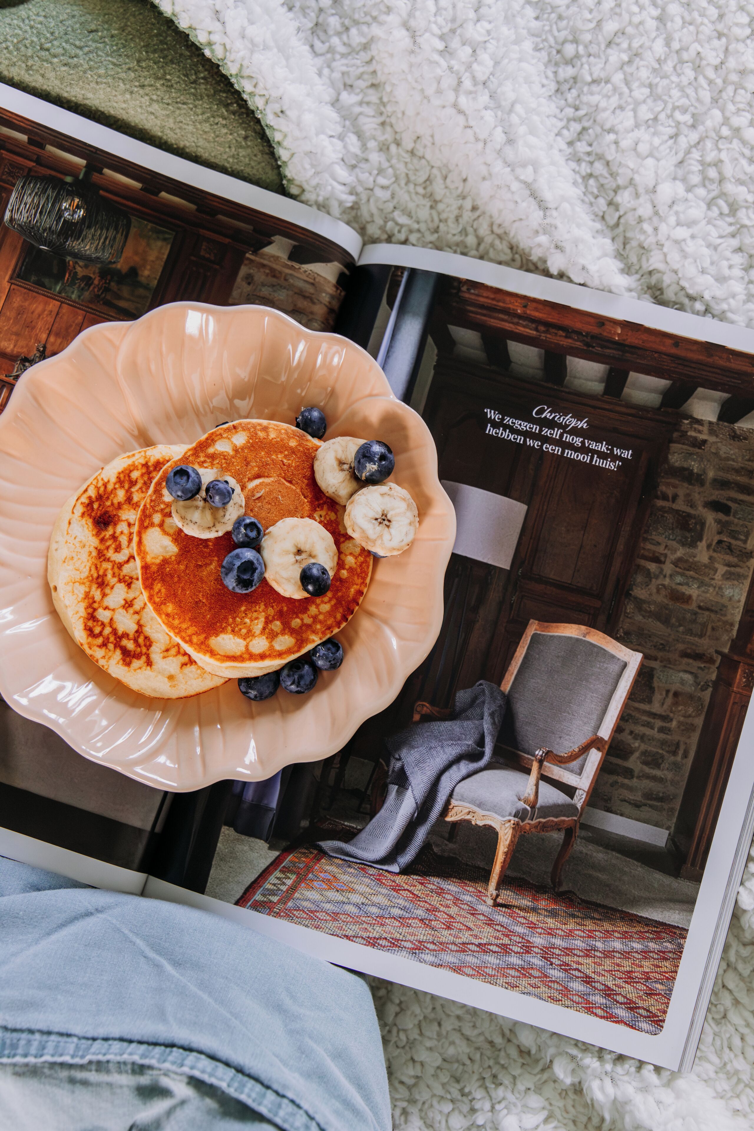 Een bladzijde uit een tijdschrift met een foto van pannenkoeken op een bord, een stoel en een interieur van een kamer.