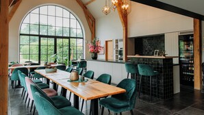 A spacious dining area with high ceilings and large windows, a bar area with stools, and a kitchen with a black tiled backsplash. - B&B Casa Cava (Dendermonde)