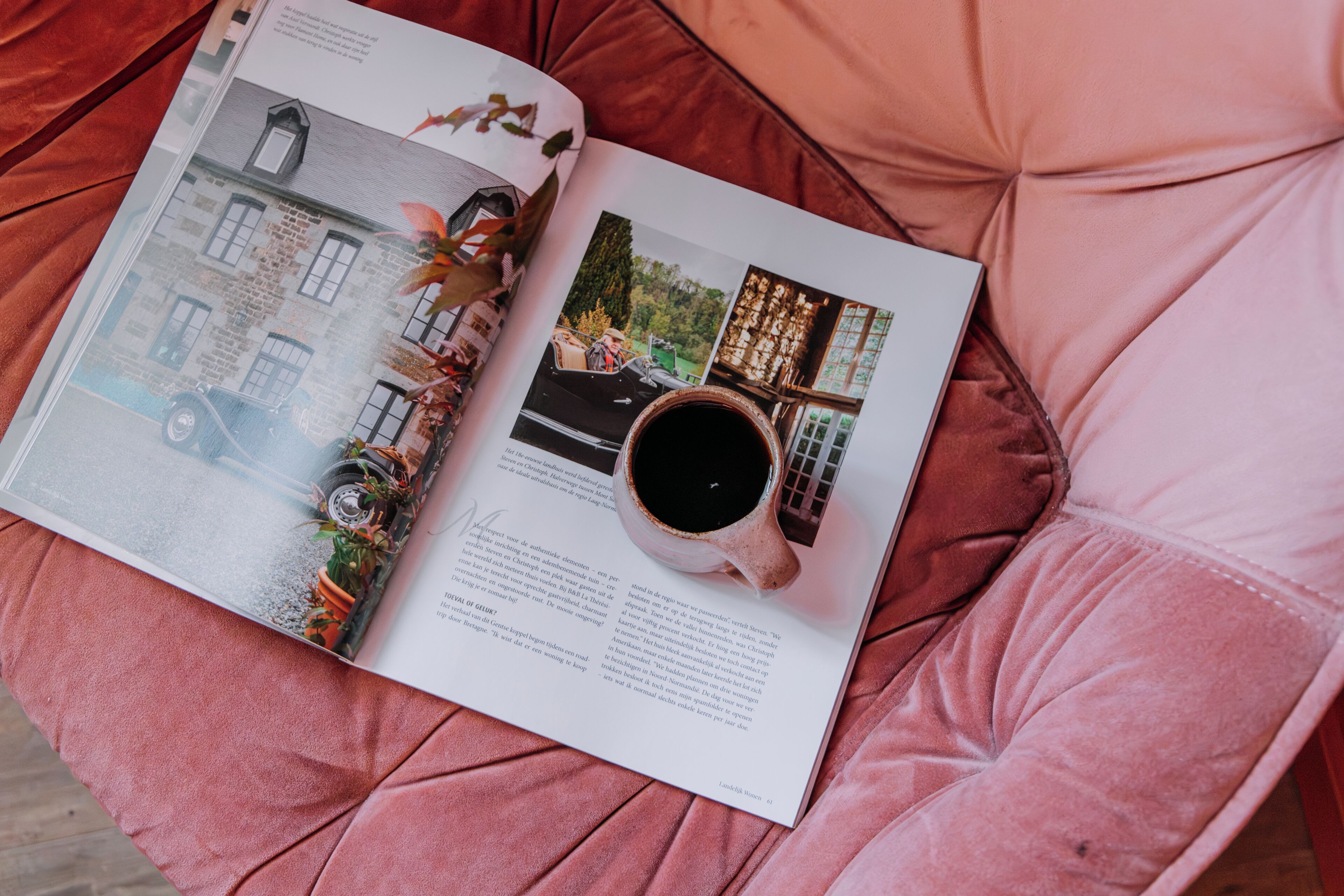 A magazine open on a pink cushioned surface, featuring a page with a vintage car, a cup of coffee, and a building.