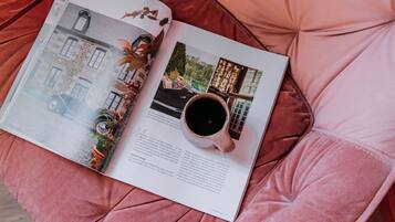 A magazine open on a pink cushioned surface, featuring a page with a vintage car, a cup of coffee, and a building.