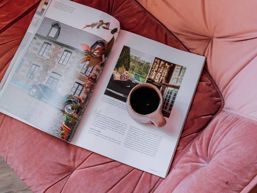A magazine open on a pink cushioned surface, featuring a page with a vintage car, a cup of coffee, and a building.