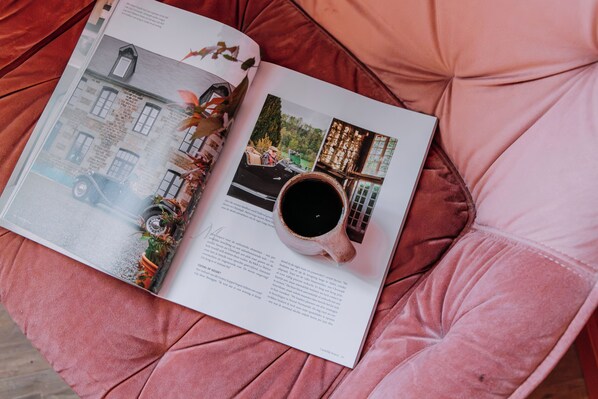 Una revista abierta sobre una superficie rosa acolchada, mostrando una página con un coche antiguo, una taza de café y un edificio.