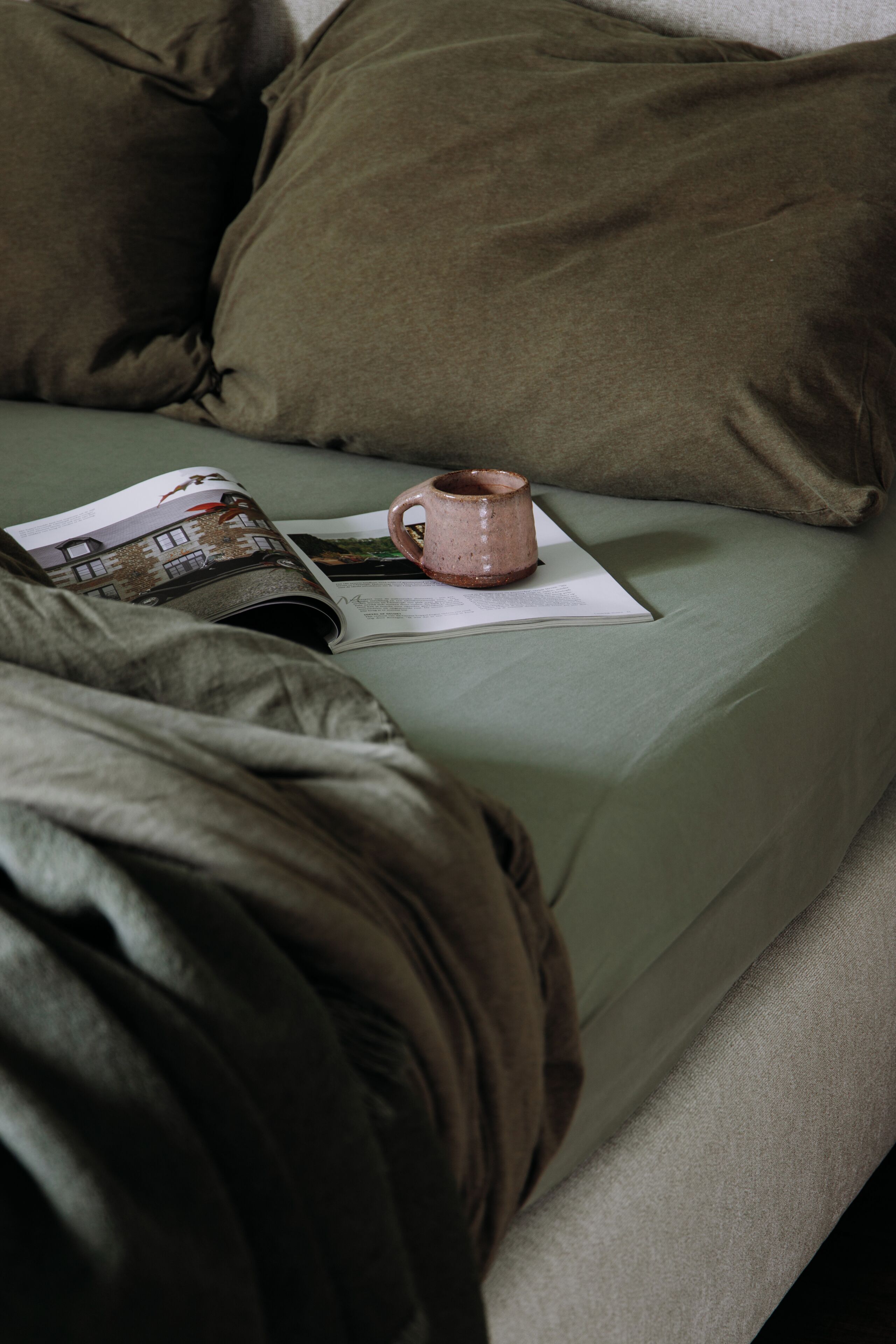 A bed with a magazine, a mug, and a pillow.