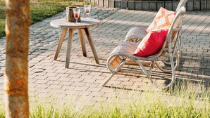 An outdoor seating area with a wicker chair and a small round table, surrounded by a stone wall and greenery. - B&B Casa Cava (Dendermonde)