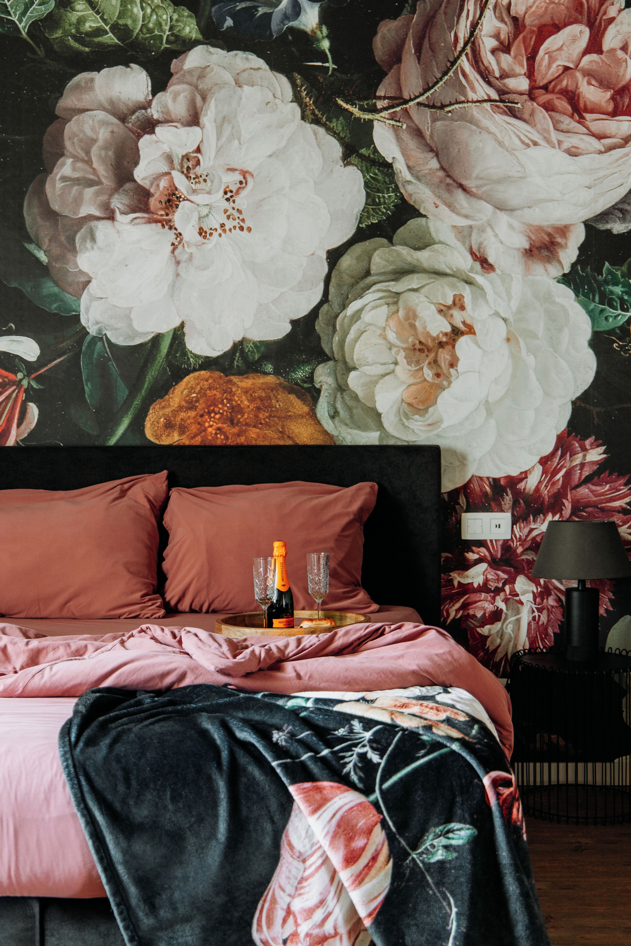 Ein Schlafzimmer mit einer großen floralen Wandmalerei, einem Bett mit pinkener Bettwäsche und einer Champagnerflasche auf dem Nachttisch.