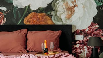 Ein Schlafzimmer mit einer großen floralen Wandmalerei, einem Bett mit pinkener Bettwäsche und einer Champagnerflasche auf dem Nachttisch.