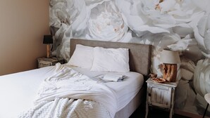 A bedroom with a large bed, a nightstand with a lamp, and a wall with a floral pattern. - B&B Casa Cava (Dendermonde)