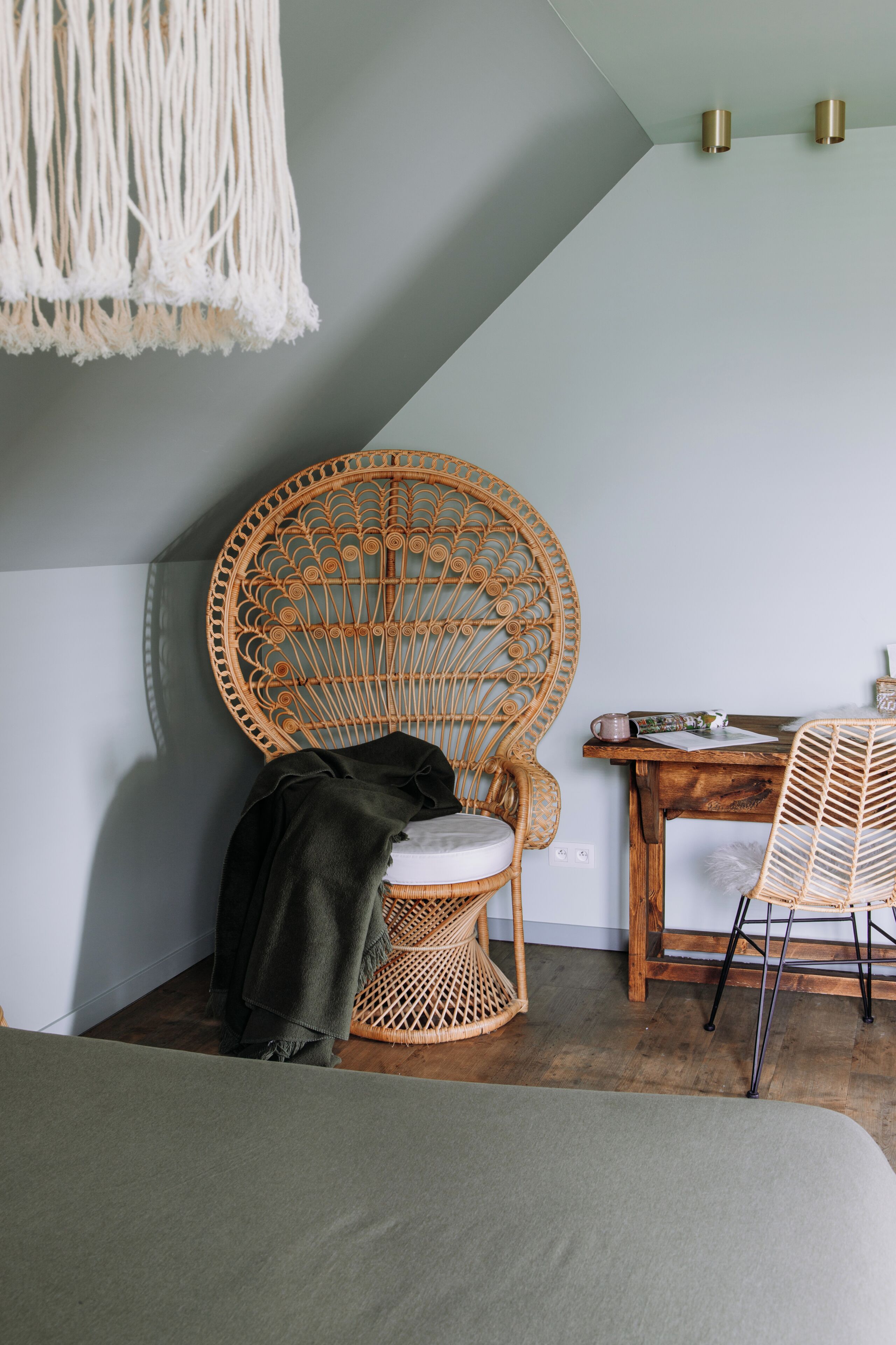 Een kamer met een rieten stoel, een houten tafel en een macramé hanglamp.