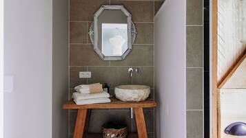 A bathroom with a stone sink, a wooden shelf with towels, a decorative mirror, and a wall-mounted light switch.