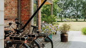 Bicycles parked against a brick wall, a potted plant, and a clear view of a grassy area. - B&B Casa Cava (Dendermonde)
