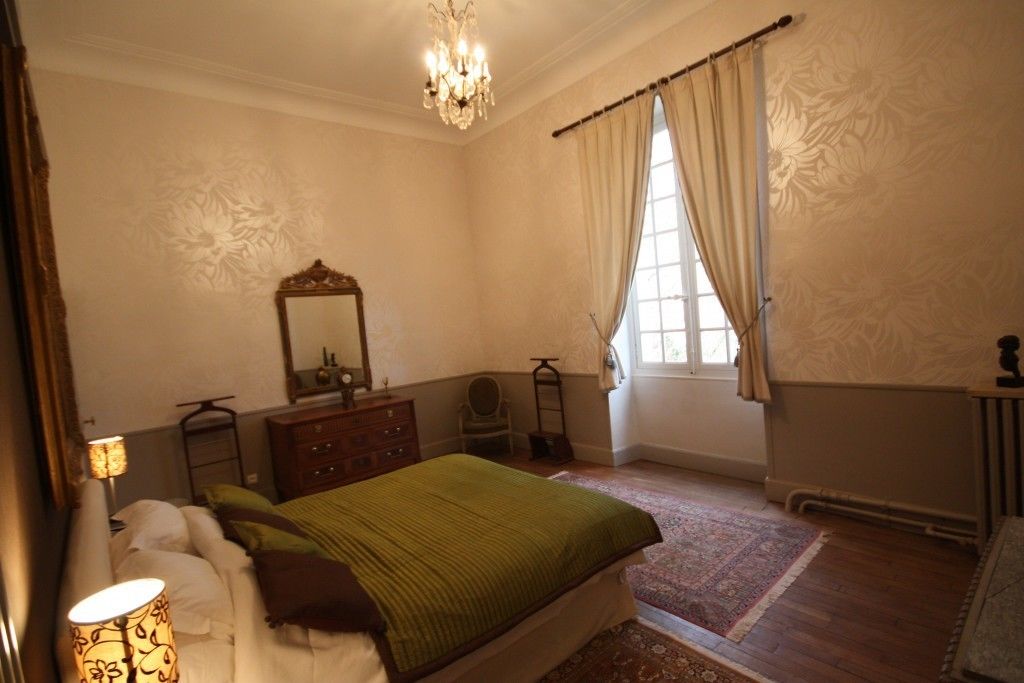 Een slaapkamer met een bed, een dressoir, een spiegel en een raam met gordijnen.