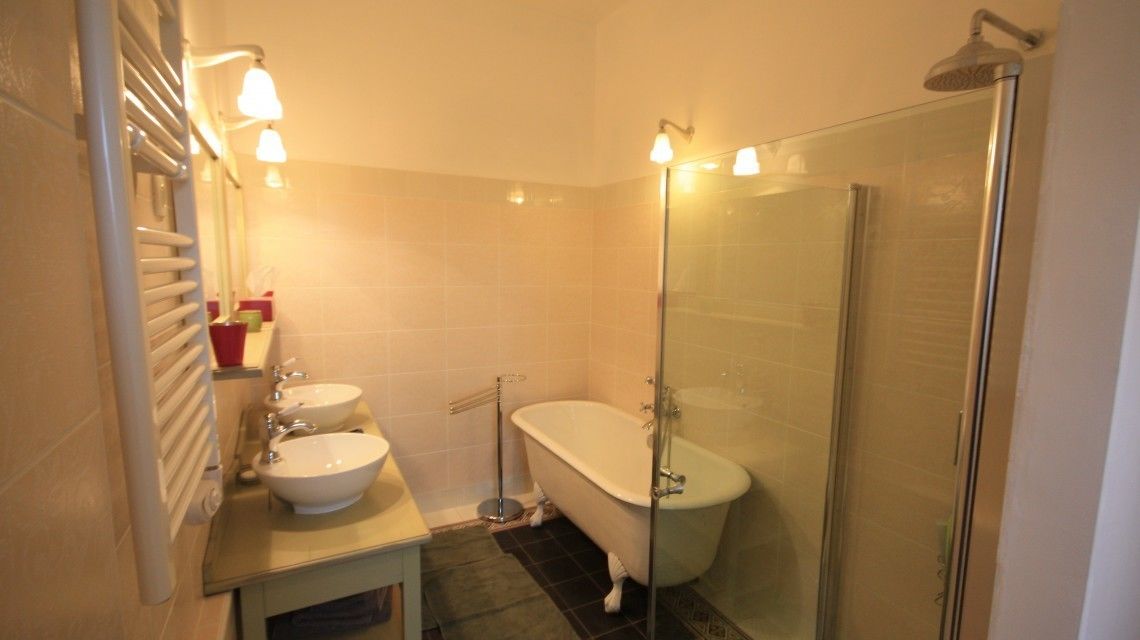 Un baño con bañera, dos lavamanos, cabina de ducha de cristal y toallero.