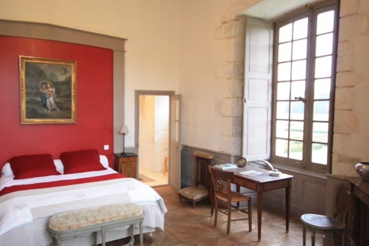 Een slaapkamer met een bed, een bureau, een stoel, een lamp en een schilderij aan de muur.