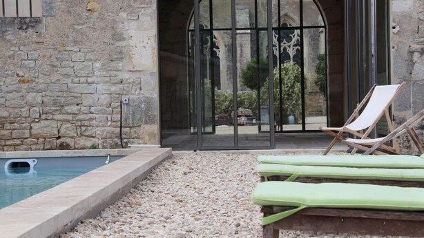 Un bâtiment en pierre doté d’une piscine, d’une porte vitrée et de deux chaises longues.