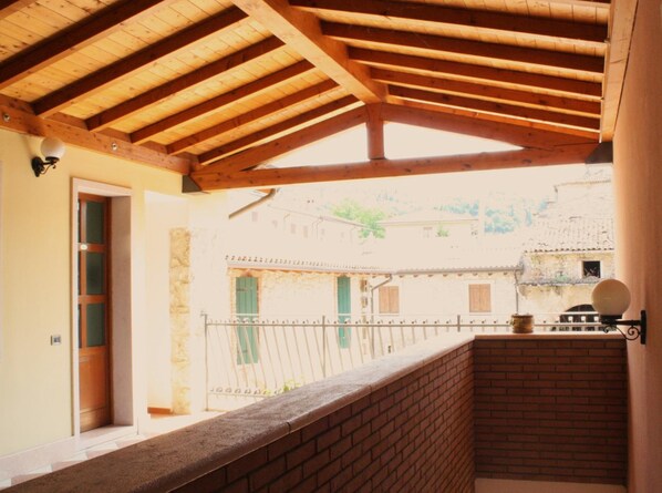 Un balcón de madera con un muro de ladrillo, una puerta y vista a un edificio tradicional con tejado de tejas.